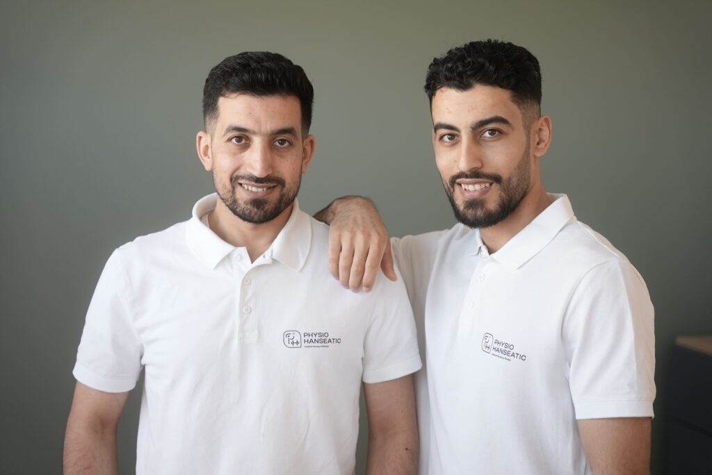 Faisal und Sleiman Hamdo stehen in weißen Poloshirts vor einem grauen Hintergrund